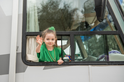 A little girl waving out the window of the Mainstreet Community Bank RV during the Mardi Gras dog parade