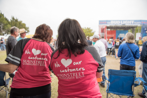 Backs of two women that have shirts that read We Love Our Customers