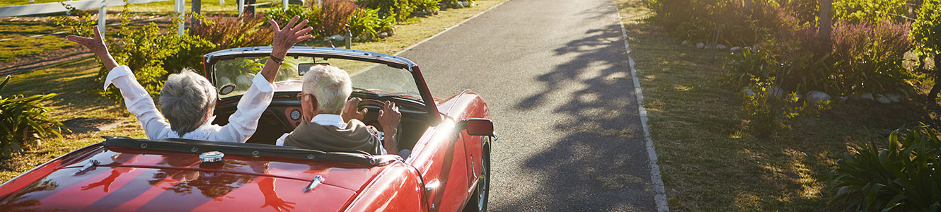 Older adults driving a convertible down a country road.