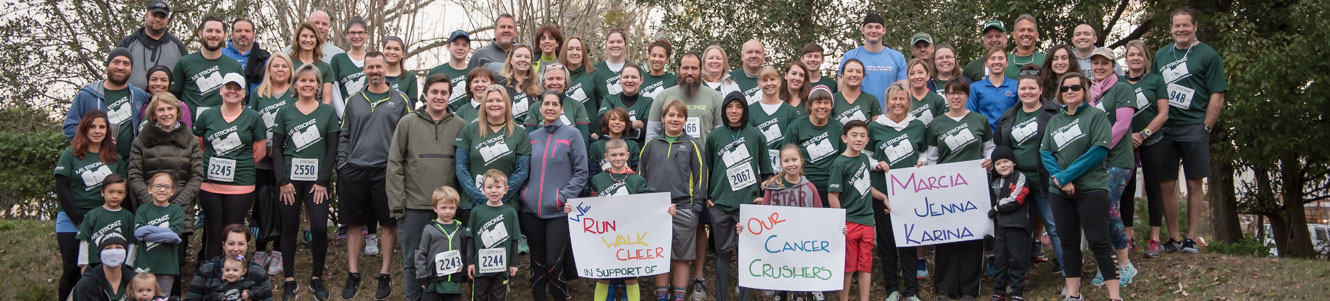 Team Mainstreet posing for a group portrait before the MeStrong 5k and holding signs of support for employees and families fighting cancer.