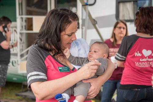 Woman holds baby while people chat in background