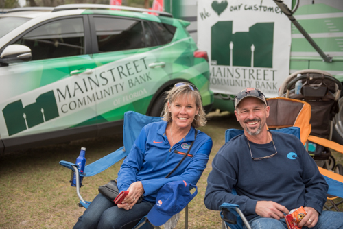 Man and woman smile for picture with Mainstreet Community Bank courier car in the background