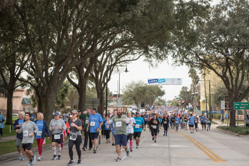 Race participants smiling and waving while running in the MeStrong 5k race in DeLand