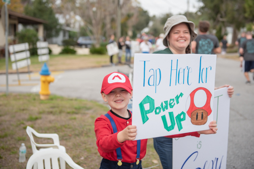 Child holding sign during race that reads "Tap Here for Power Up"