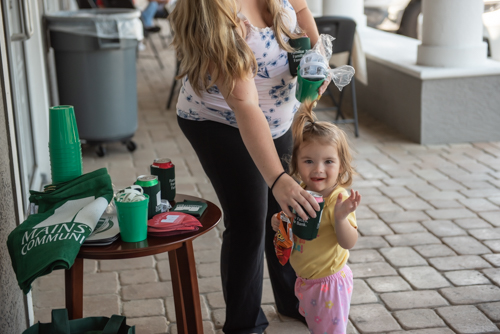 Small child waving while mother hands her drink at Mainstreet Community Bank event