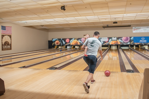 Man bowling with happy little girl in his arms