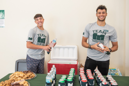 Two young men, one making a silly face while they put water in coozies at teacher's lunch hosted by Mainstreet Community Bank