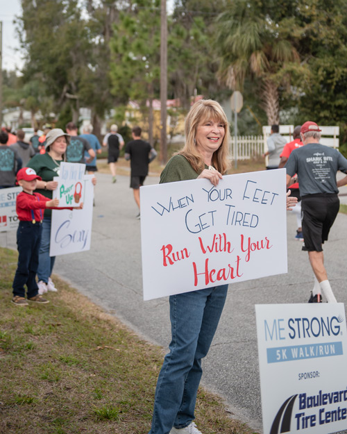 Team Mainstreet member holds sign and cheers on runners during MeStrong