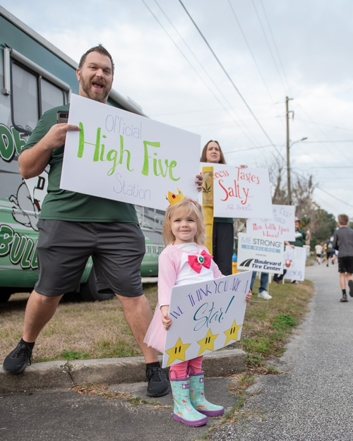 Man and little girl hold signs for runners during MeStrong race