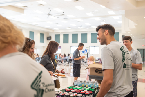 A man laughs with a teacher as a young man looks on while serving drinks at DeLand High School